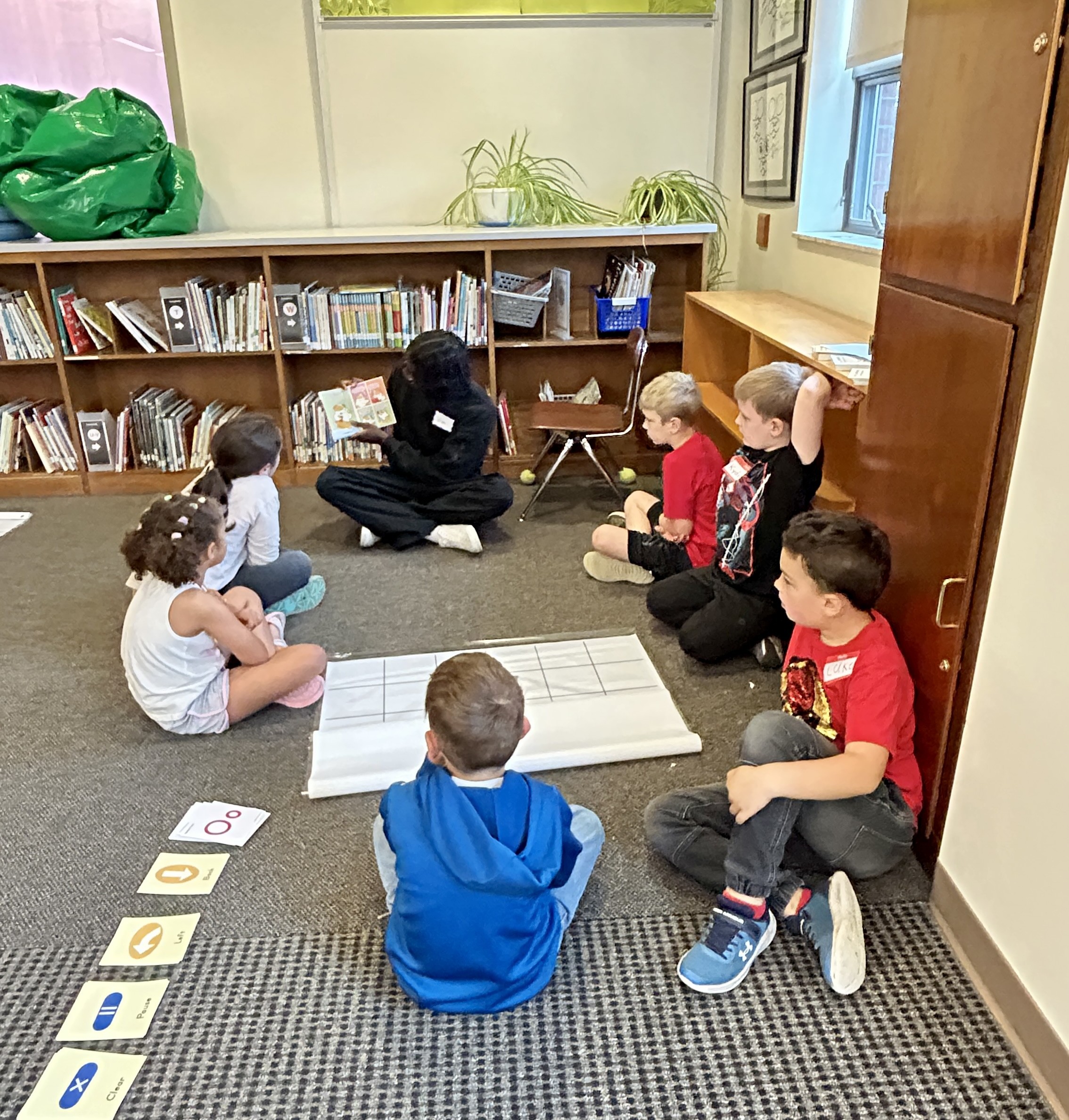 Picture of stidents (sittin in a circle) being read to by an Outreach Fellow.