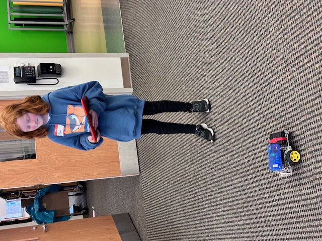 Picture of one of the students (standing) demonstrating using an IPAD to control a robot.